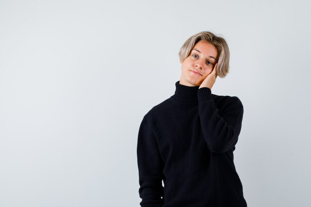 Portrait of cute teen boy leaning cheek on hand in turtleneck sweater and looking dreamy front view