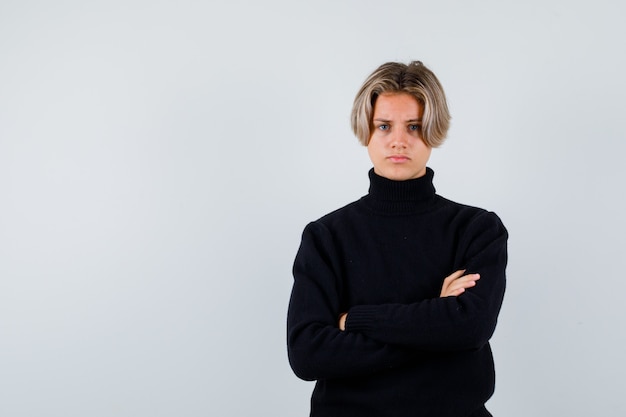 Portrait of cute teen boy with arms folded in black turtleneck sweater and looking spiteful front view