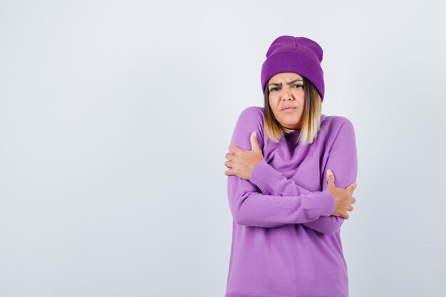 Portrait of cute woman hugging herself, feeling cold in sweater, beanie and looking gloomy front view