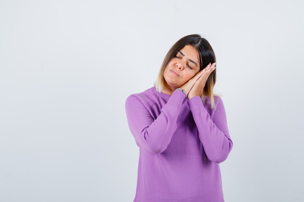 Portrait of cute woman leaning on palms as pillow in purple sweater and looking sleepy front view