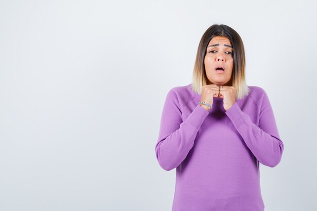 Portrait of cute woman with hands under chin in purple sweater and looking puzzled front view