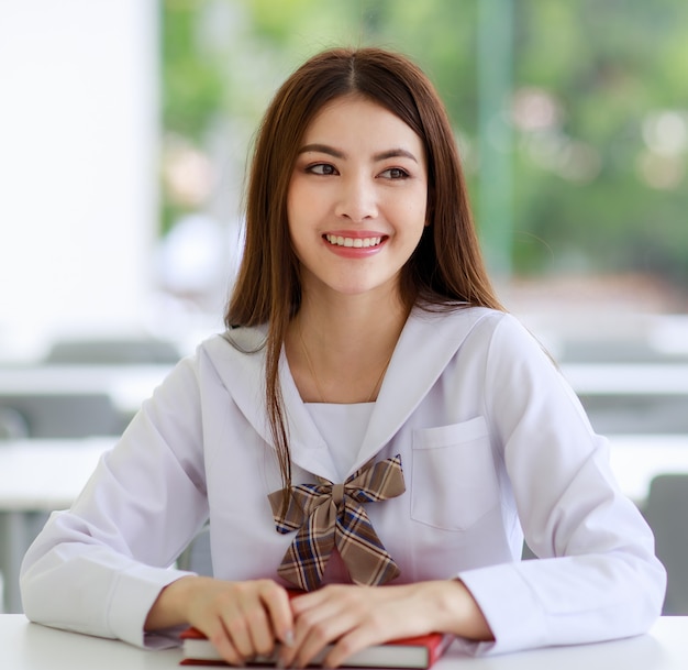 Premium Photo | Portrait of cute and young asian girl, lao ethnicity,  wearing japanese, korean style schoolgirl uniform, sitting pose smile to  camera with cheerful and confident.