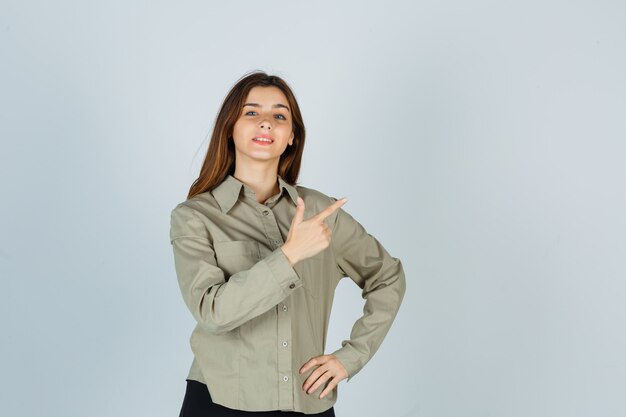 Portrait of cute young female pointing at upper right corner in shirt and looking proud front view