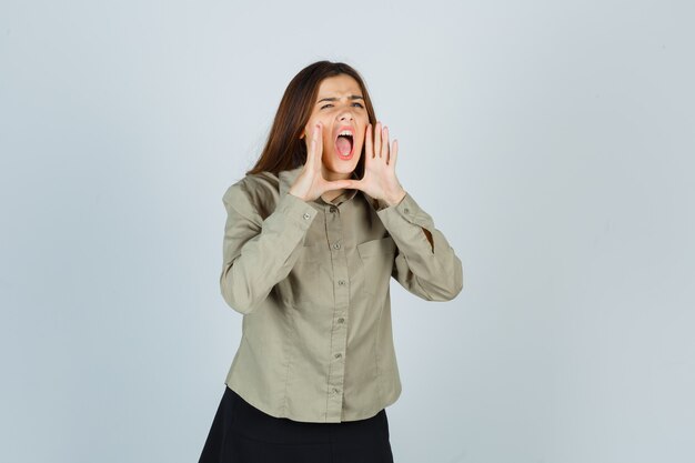 Portrait of cute young female shouting or announcing something in shirt, skirt and looking excited front view