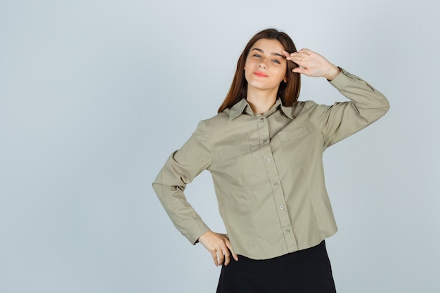 Ritratto di giovane donna carina che mostra gesto di saluto in camicia, gonna e guarda orgogliosa vista frontale