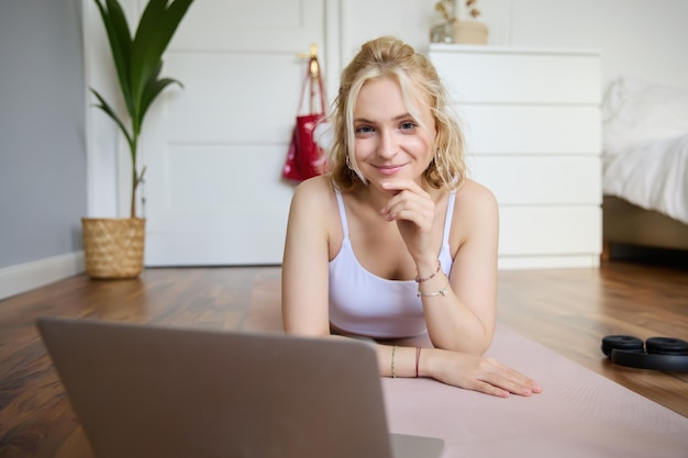 Ritratto di una bella giovane donna in fitness che si allena a casa sdraiata su un tappetino da yoga di gomma che guarda