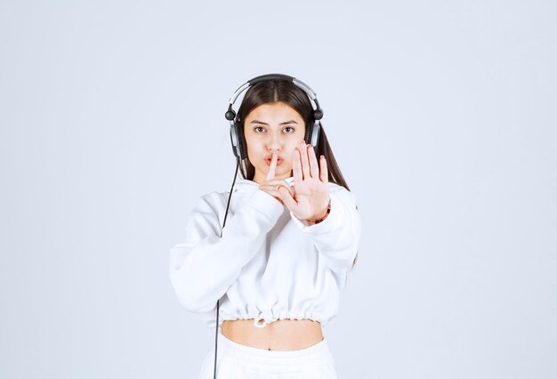 Portrait of a cute young girl model with headphones showing silent sign.