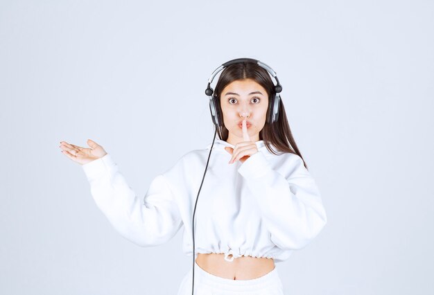 Portrait of a cute young girl model with headphones showing silent sign.