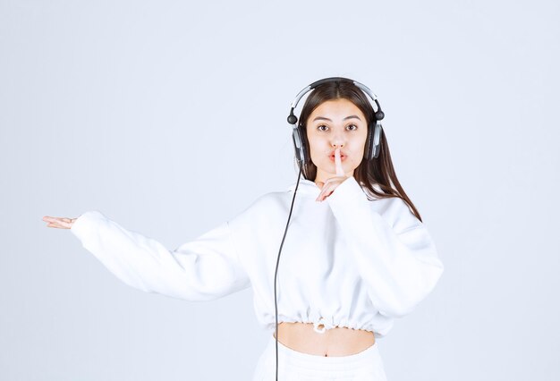 Portrait of a cute young girl model with headphones showing silent sign .