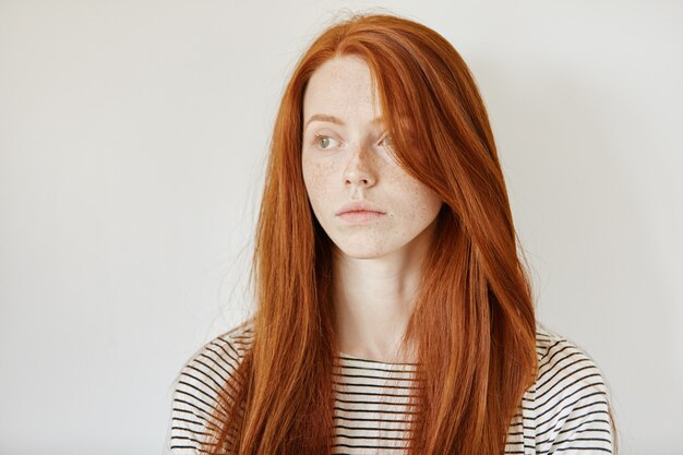 Portrait of cute young redhead Caucasian woman with freckles and long loose hair posing