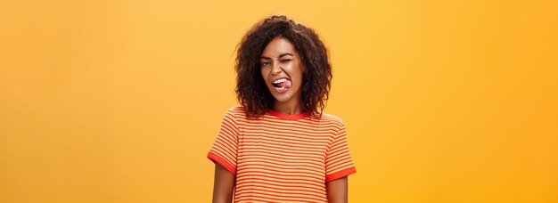 Portrait of daring and emotive confident flirty woman with afro hairstyle winking joyfully showing t