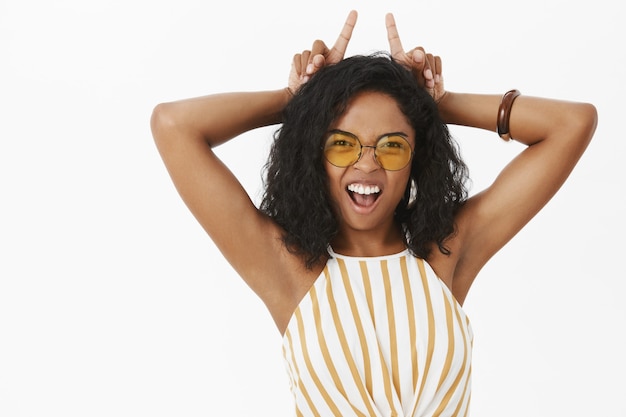 Free photo portrait of daring energized and confident funny young african american woman in sunglasses and striped top showing teeth