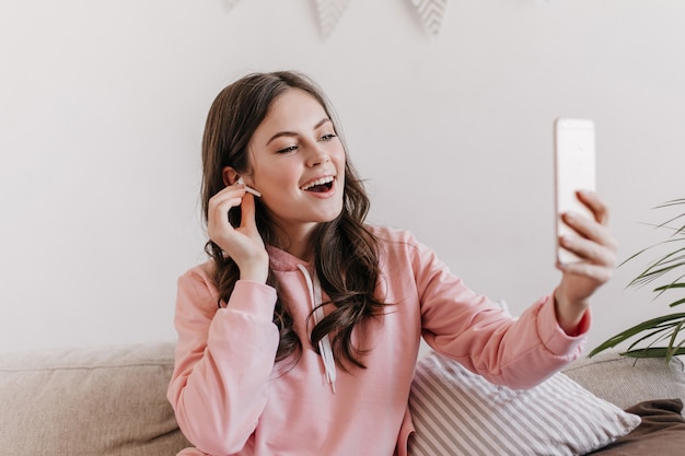 Portrait of dark-haired woman in pink hoodie talking via video link in smartphone