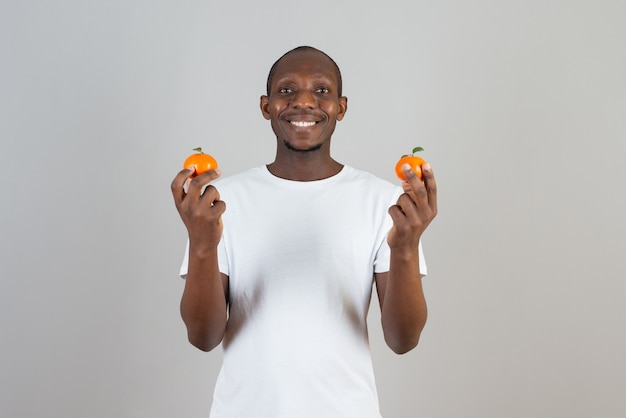 Портрет темнокожего мужчины в белой футболке, держащего мандарины на серой стене