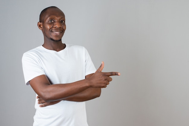 Portrait of dark skinned man in white t-shirt standing on gray wall