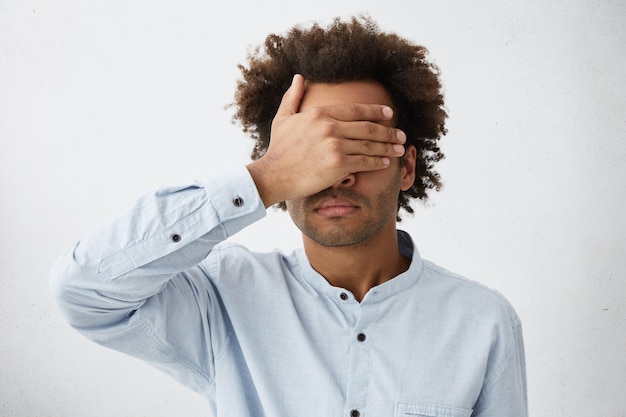 Portrait of dark-skinned mixed race man with bushy hairstyle wearing white T-shirt covering his face