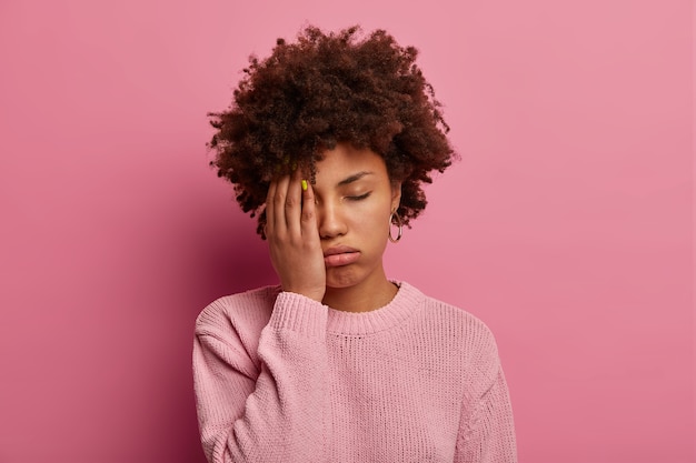 Portrait of dark skinned woman covers half of face, sighs from tiredness