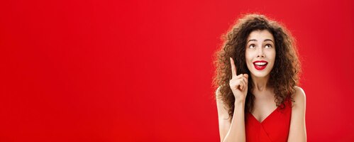Free photo portrait of delighted charming silly female with curly hairstyle in dress raising index finger in eu