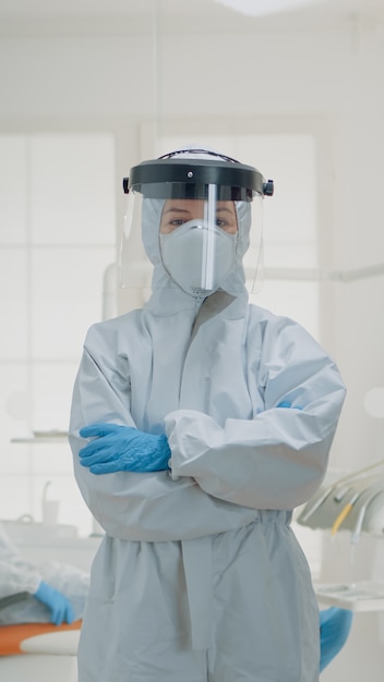 Portrait of dentist standing in hazmat suit for virus protection at oral clinic. Caucasian woman wearing coverall ppe prepared for dentistry operation and surgical consultation