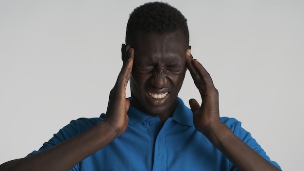 白い背景の上のカメラで頭痛を示す落ち込んでアフリカ系アメリカ人の男の肖像画。痛みの表現
