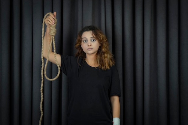 Portrait of depressed young girl holding Hangman's knot and looking at camera. High quality photo