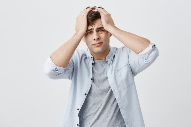 Portrait of desperate annoyed tired european guy frowning his face, putting hands on his head, remembering that he forgot about something. Negative human face expressions, emotions and feelings