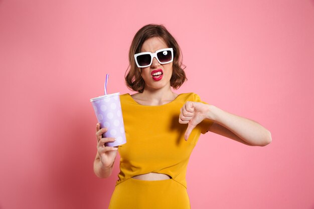 Portrait of a disappointed girl in sunglasses holding cup