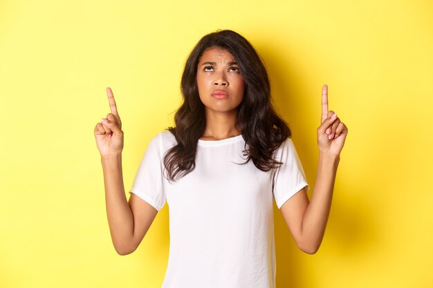 Portrait of disappointed and sad africanamerican girl pointing and looking up frowning displeased