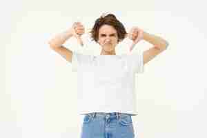 Free photo portrait of disappointed young woman female client shows dislike gesture thumbs down stands over