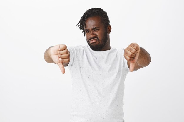 Portrait of disgusted guy with braids posing against the white wall