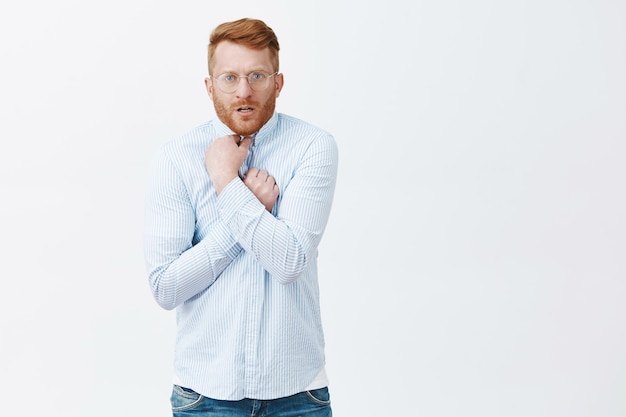 Portrait of displeased embarrassed and intense redhead guy with bristle in glasses pulling shirt on chest