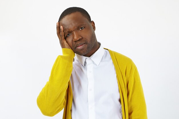 Portrait of displeased frustrated African man feeling unwell and sick, touching head because of migraine or toothache after stressful day at work, posing isolated at blank studio wall background