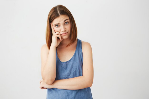 Portrait of displeased young brunette girl with finger on temple thinking .