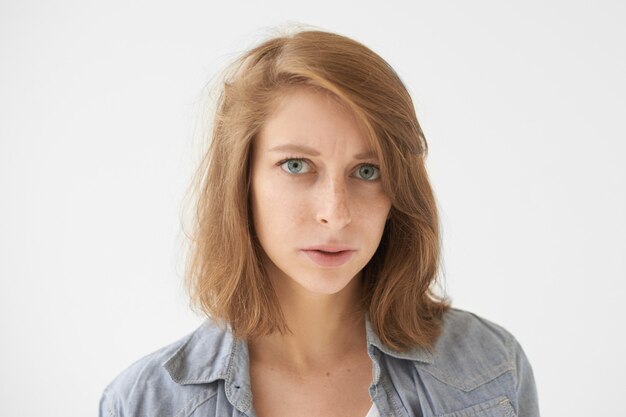 Portrait of displeased young Caucasian female with freckles and blue eyes frowning brows having sullen strict facial expression. Human emotions, reaction, feelings, life perception and attitude