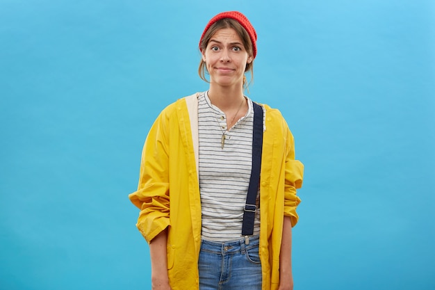 Portrait of dissatisfied woman wearing red hat, yellow raincoat and overalls frowning her face having bad mood as her husband didn't take her on lake to go fishing. Facial expressions and emotions