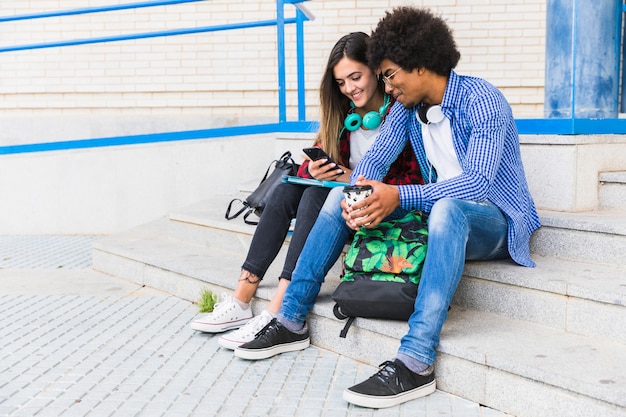Портрет разнообразных подростков мужского и женского пола студентов, сидя на ступеньках с помощью мобильного телефона