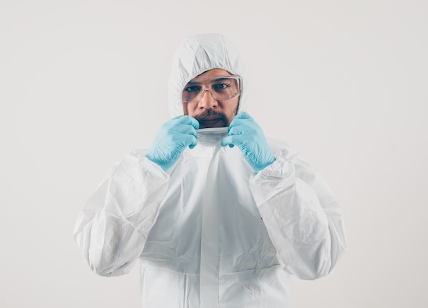 Free photo portrait of a doctor at light background standing and holding his suit in mask, medical gloves and protective suit .