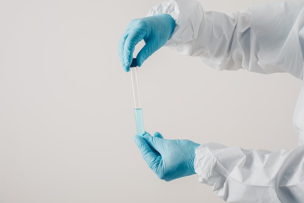 Portrait of a doctor at light background standing and holding medicine in medical gloves and protective suit