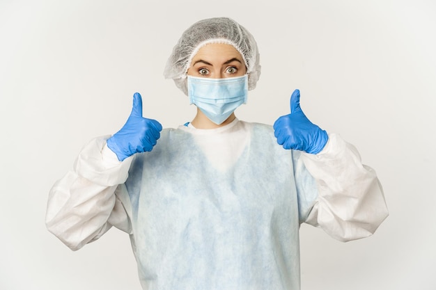 Portrait of doctor in personal protective equipment showing thumbs up wearing face mask concept of c...