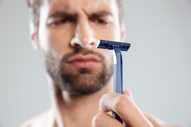 Portrait of a doubtful concentrated bearded man looking at razor