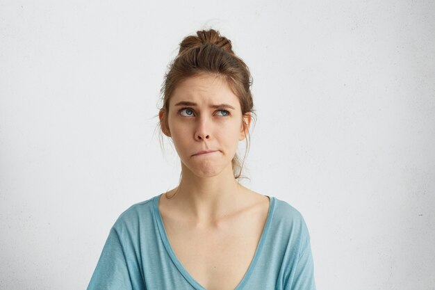 Portrait of doubtful and pensive woman looking up and curving her lips trying to make decision. Irresolute female thinking something over