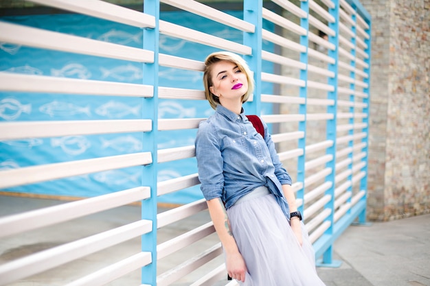 Portrait of dreamy blond woman with short hair, bright pink lips and blue eyes wearing blue denim shirt