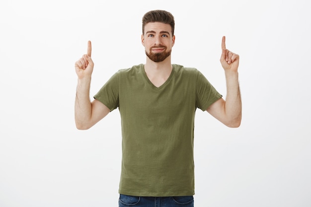 Portrait of dreamy delighted and cute bearded boyfriend in love smirking pleased, pointing up