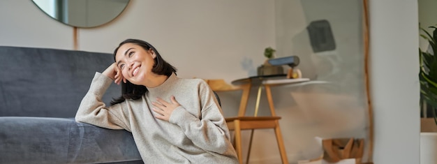 Free photo portrait of dreamy woman sitting with laptop on floor watching on computer and drinking coffee