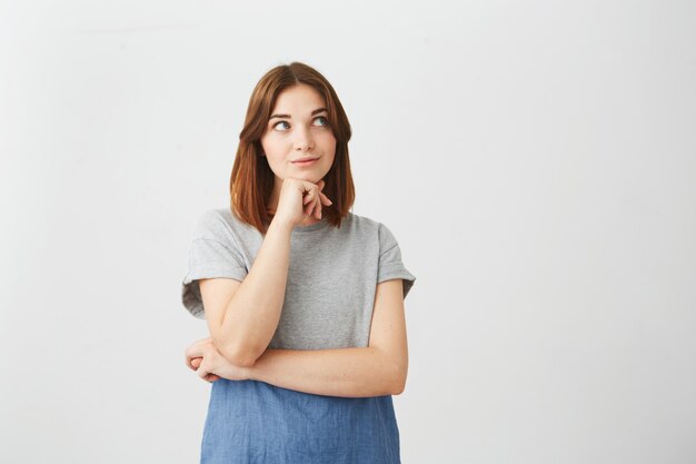 Portrait of dreamy young beautiful girl smiling looking up thinking dreaming with hand on chin .