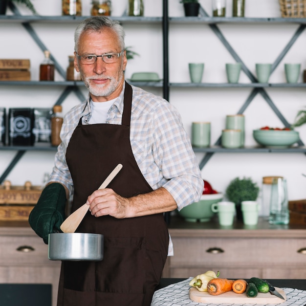 Portrait of an elderly man preparing food standing in front of table with vegetable