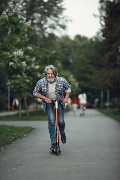 Portrait of elderly man with kick scooter in a summer park