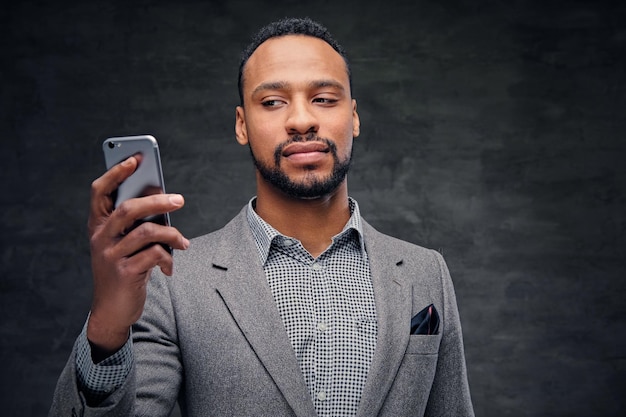 Portrait of elegant bearded black American male in a grey suit holds smart phone.