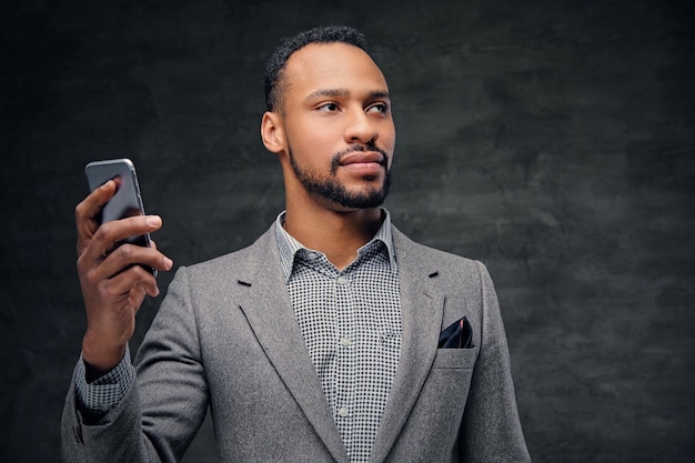灰色のスーツを着たエレガントなひげを生やした黒人のアメリカ人男性の肖像画は、スマートフォンを保持しています。