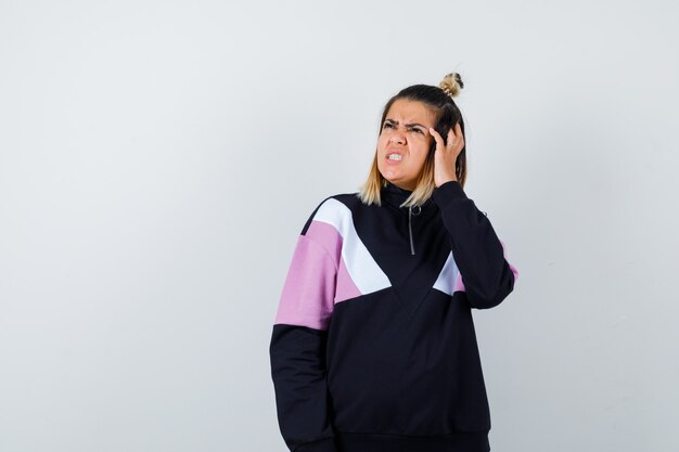 Portrait of elegant lady holding hand on head, looking up in sweatshirt and looking sullen